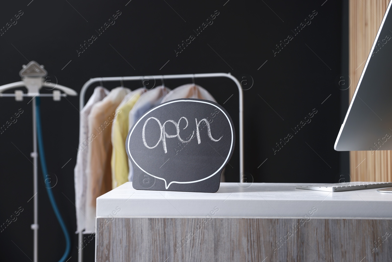 Photo of Dry-cleaning service. Open sign and computer on white counter indoors