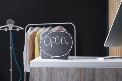 Photo of Dry-cleaning service. Open sign and computer on white counter indoors