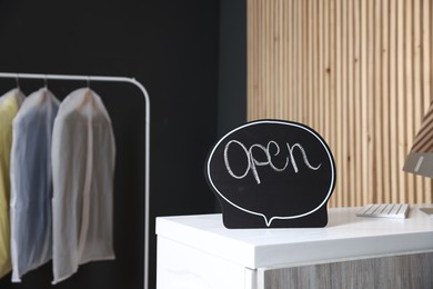 Photo of Dry-cleaning service. Open sign on white counter indoors, space for text