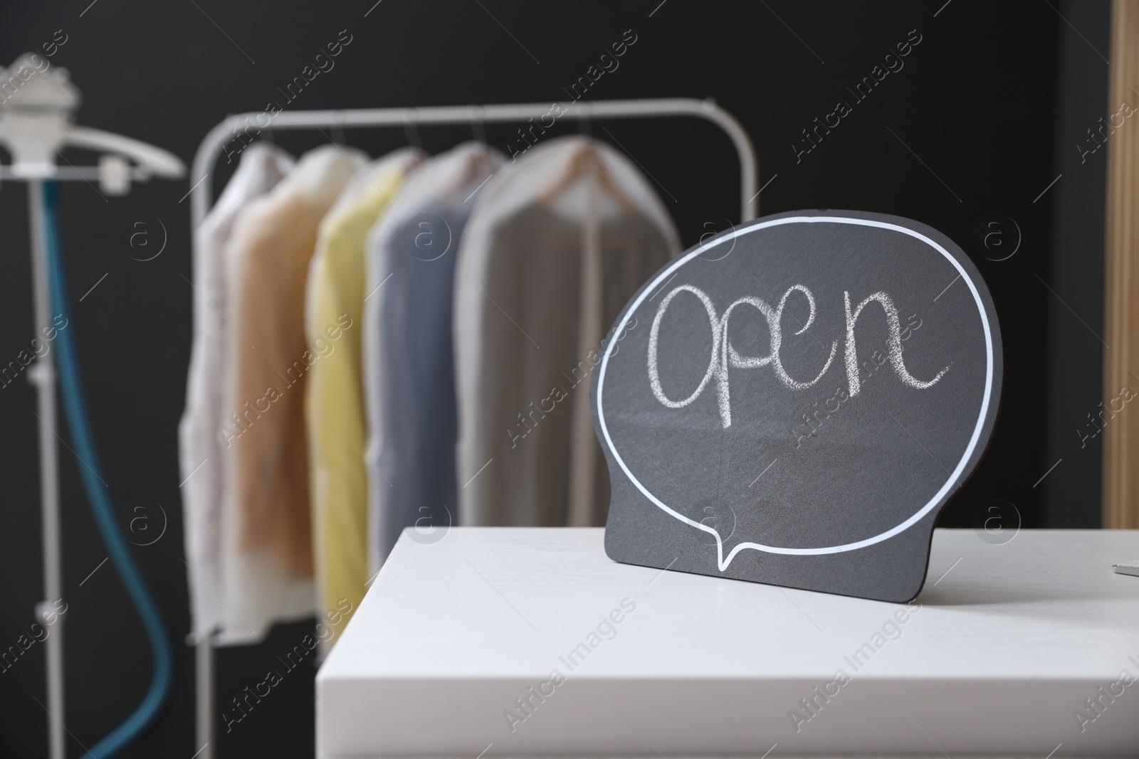 Photo of Dry-cleaning service. Open sign on white counter indoors, closeup. Space for text