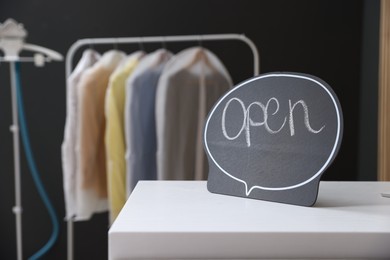 Photo of Dry-cleaning service. Open sign on white counter indoors, closeup. Space for text