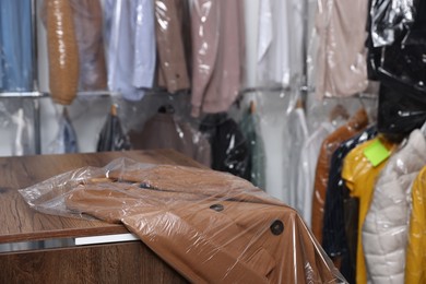 Photo of Dry-cleaning service. Clean jacket in plastic bag on counter indoors, closeup