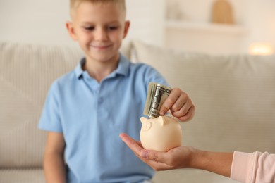 Photo of Mother and her son putting pocket money into piggy bank at home, closeup