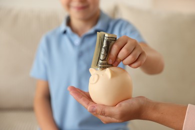 Photo of Mother and her son putting pocket money into piggy bank at home, closeup