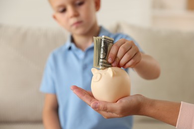 Photo of Mother and her son putting pocket money into piggy bank at home, closeup