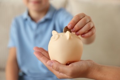 Photo of Mother and her son putting pocket money into piggy bank at home, closeup
