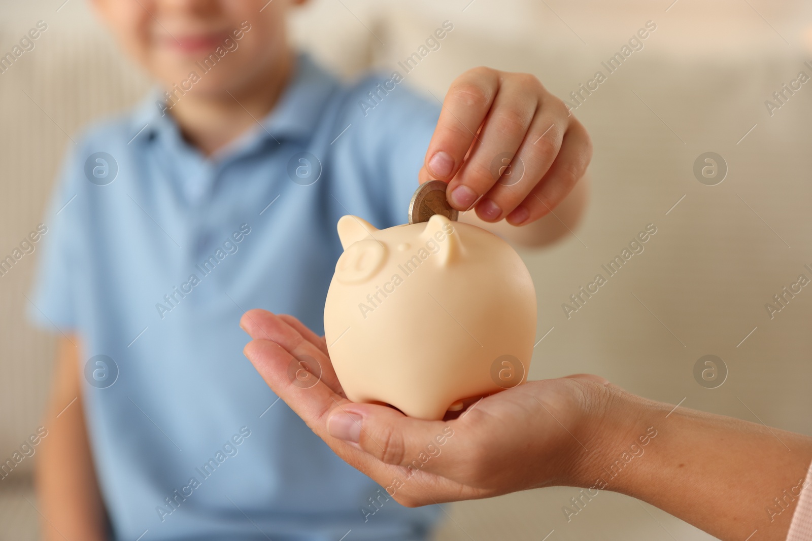 Photo of Mother and her son putting pocket money into piggy bank at home, closeup