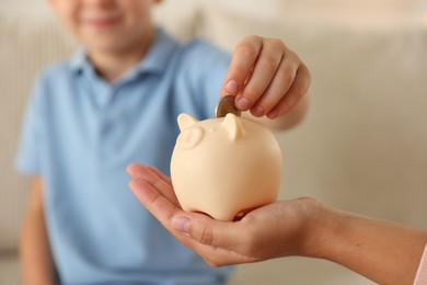 Photo of Mother and her son putting pocket money into piggy bank at home, closeup