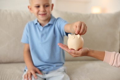 Photo of Mother and her son putting pocket money into piggy bank at home, closeup