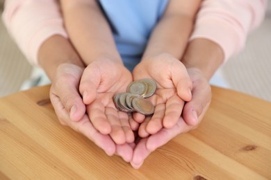 Photo of Pocket money. Mother and her son holding coins at wooden table, closeup