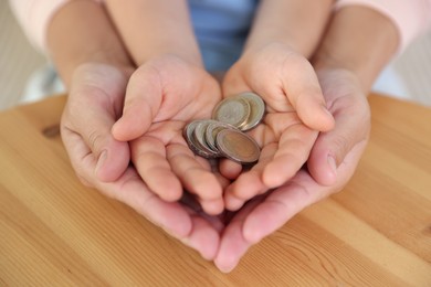 Photo of Pocket money. Mother and her son holding coins at wooden table, closeup