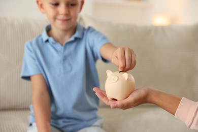 Photo of Mother and her son putting pocket money into piggy bank at home, closeup