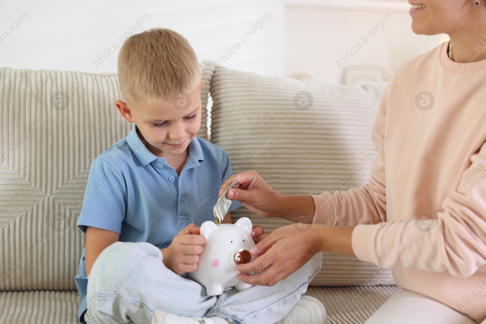 Photo of Mother and her son putting pocket money into piggy bank at home, closeup