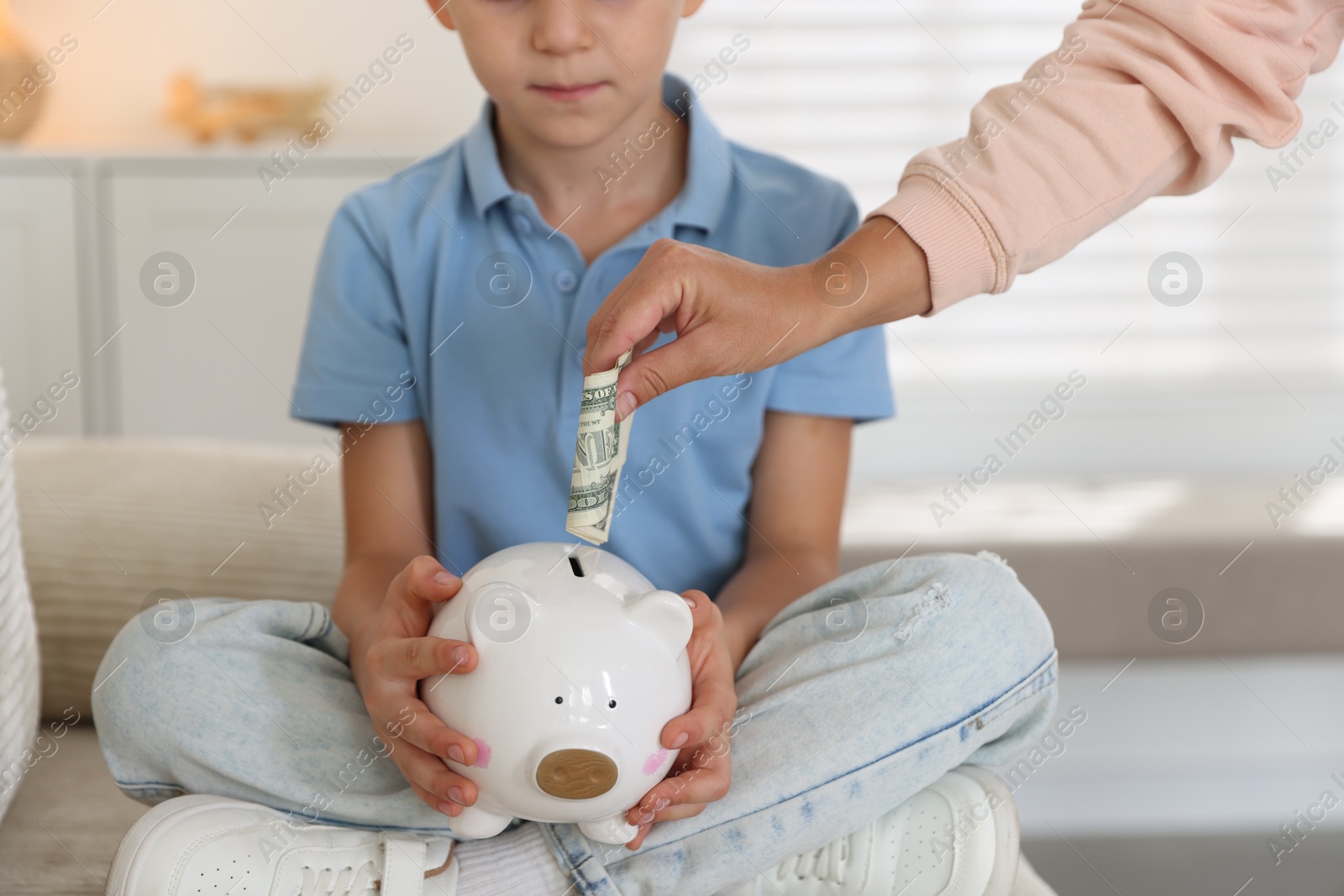 Photo of Mother and her son putting pocket money into piggy bank at home, closeup