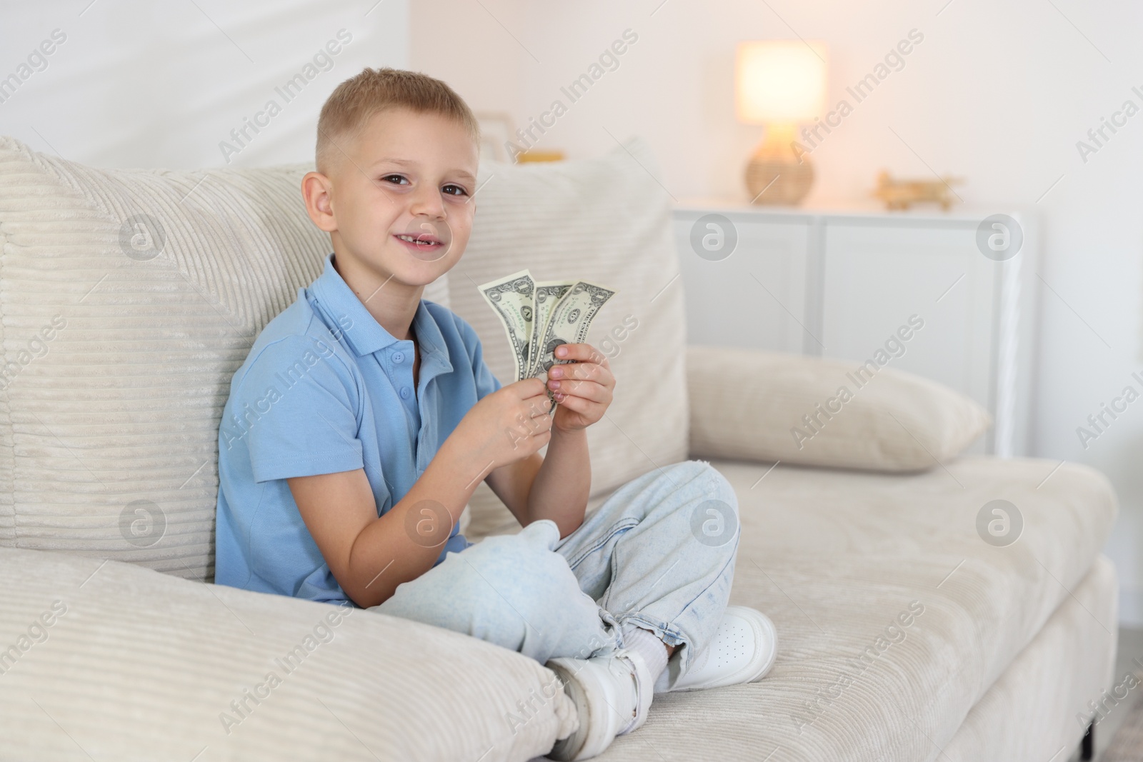 Photo of Little boy holding pocket money on sofa at home