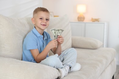 Photo of Little boy holding pocket money on sofa at home