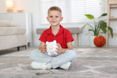 Photo of Little boy with pocket money and piggy bank on floor at home