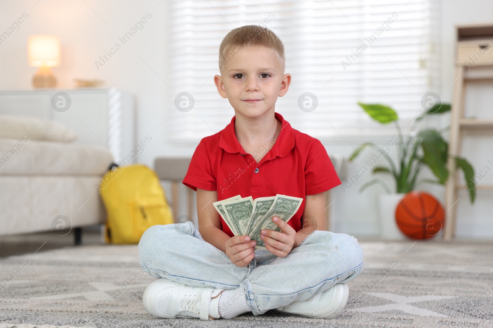 Photo of Little boy holding pocket money on floor at home