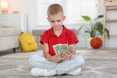Photo of Little boy holding pocket money on floor at home