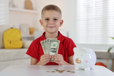 Photo of Little boy with pocket money and piggy bank at white table indoors