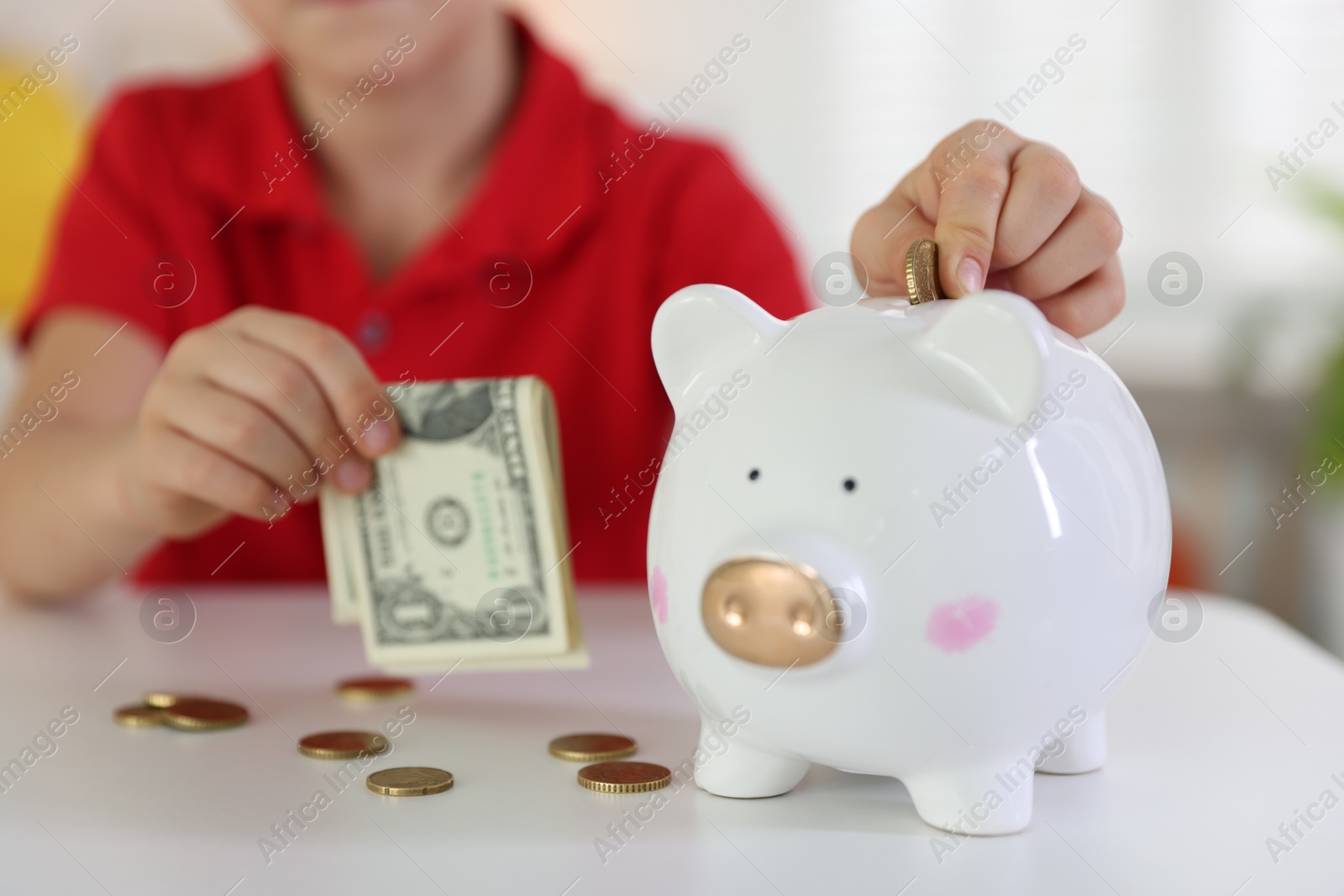 Photo of Little boy putting pocket money into piggy bank at white table indoors, closeup