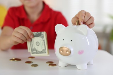 Photo of Little boy putting pocket money into piggy bank at white table indoors, closeup