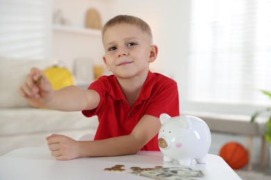 Photo of Little boy with pocket money and piggy bank at white table indoors
