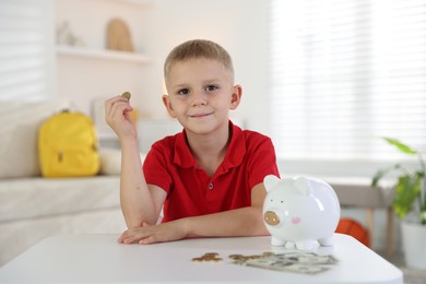 Photo of Little boy with pocket money and piggy bank at white table indoors