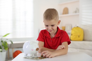 Photo of Little boy with pocket money and piggy bank at white table indoors