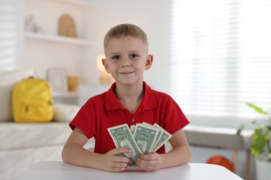 Photo of Little boy holding pocket money at white table indoors