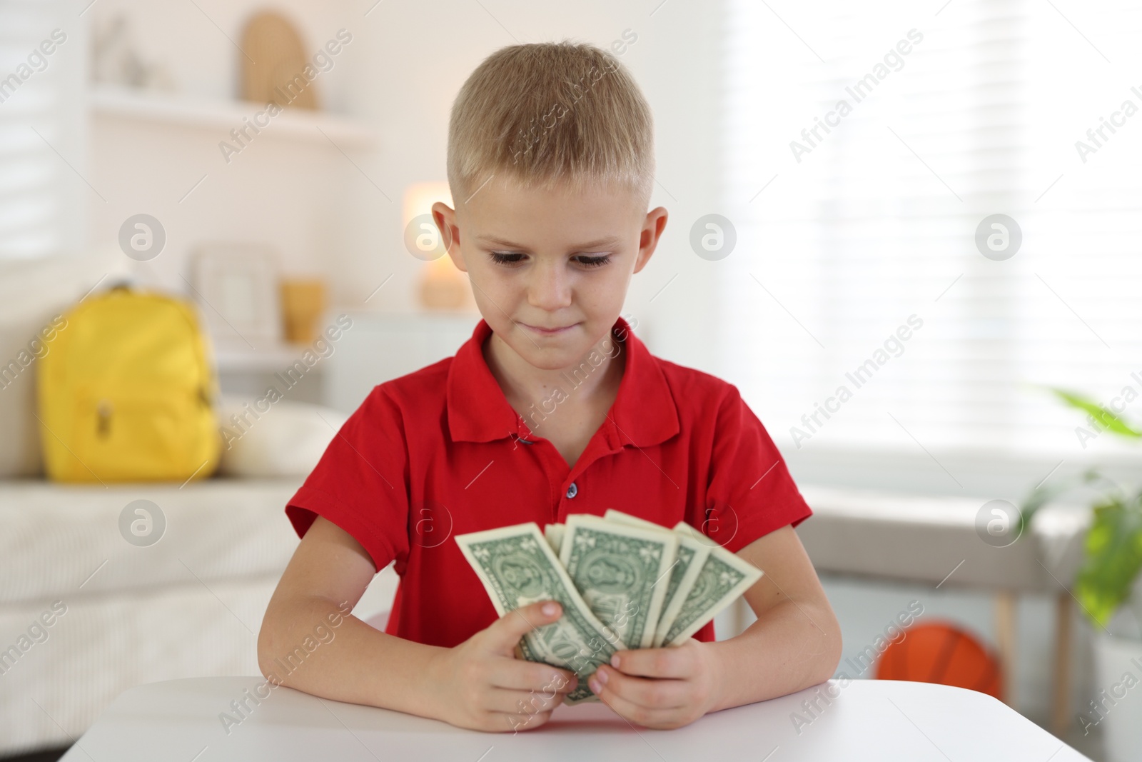 Photo of Little boy holding pocket money at white table indoors