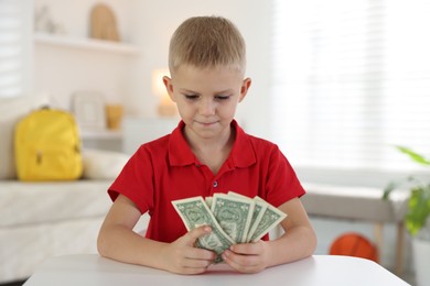 Photo of Little boy holding pocket money at white table indoors