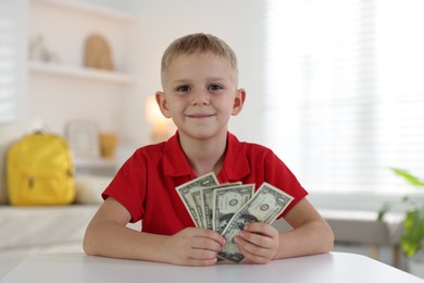 Photo of Little boy holding pocket money at white table indoors