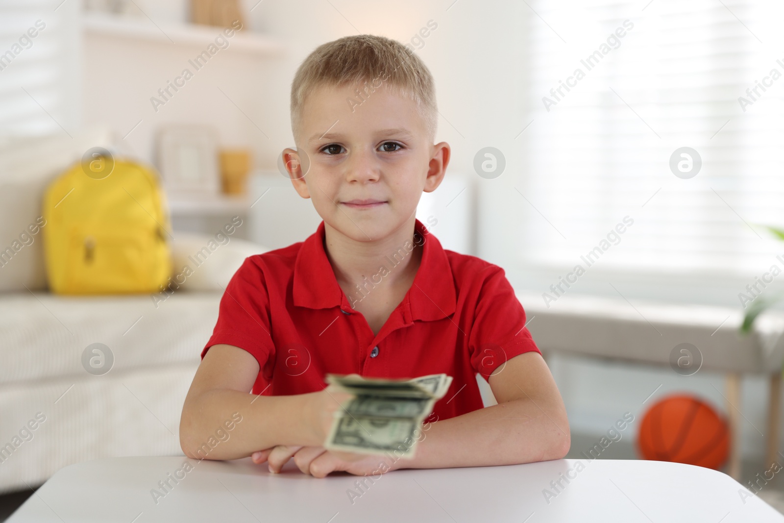 Photo of Little boy holding pocket money at white table indoors