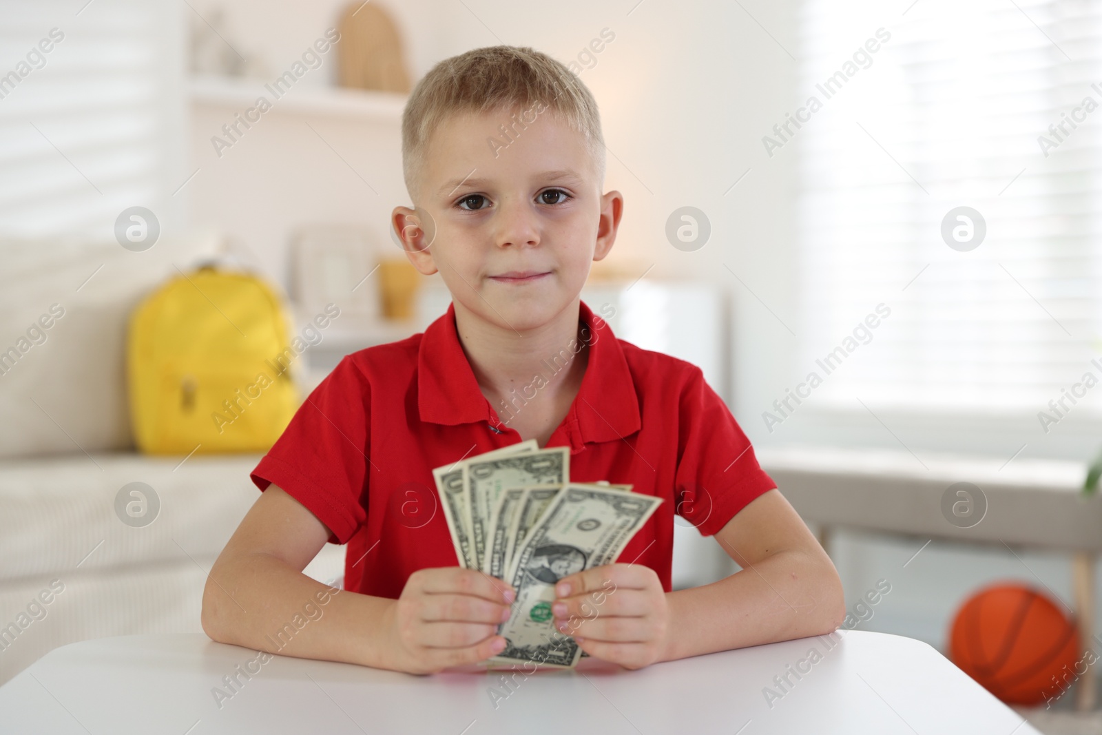 Photo of Little boy holding pocket money at white table indoors