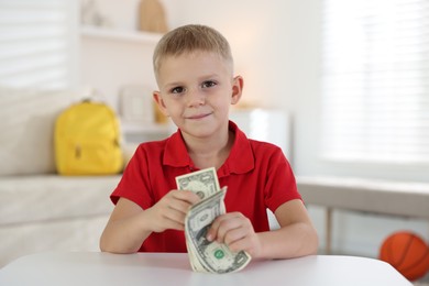 Photo of Little boy holding pocket money at white table indoors