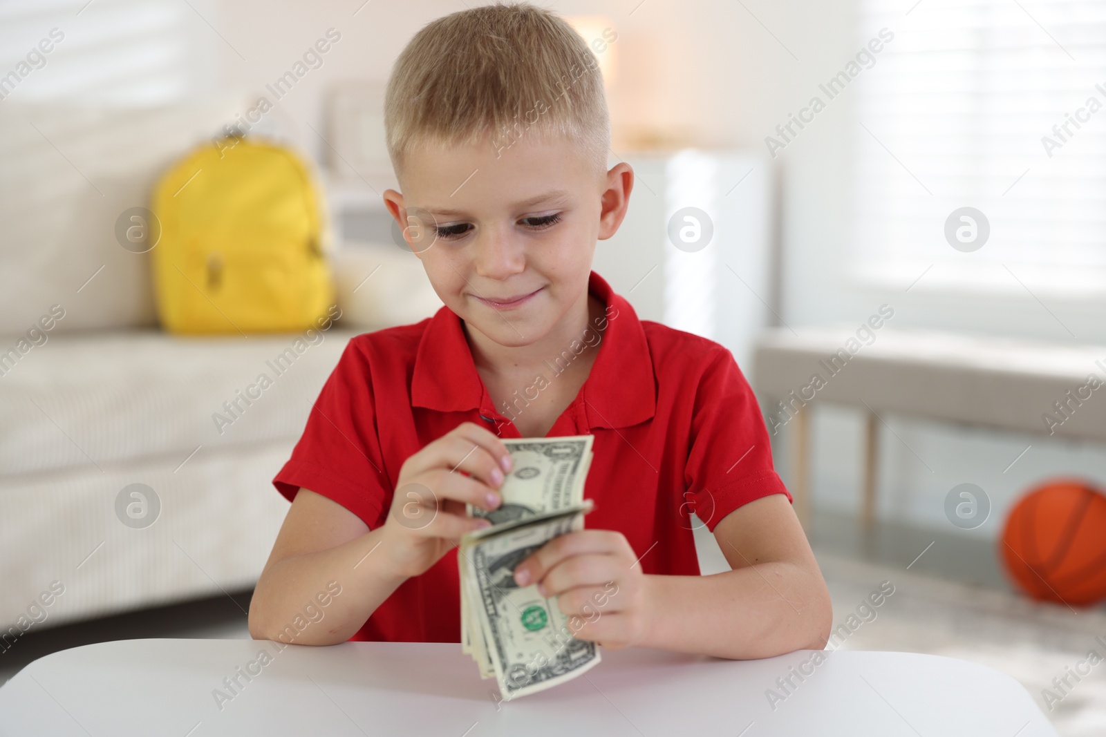 Photo of Little boy holding pocket money at white table indoors