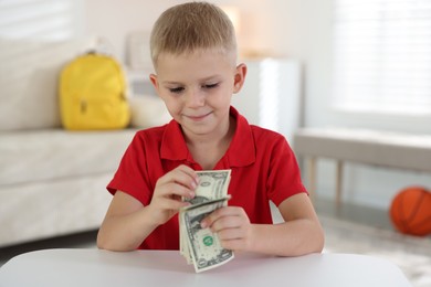 Photo of Little boy holding pocket money at white table indoors