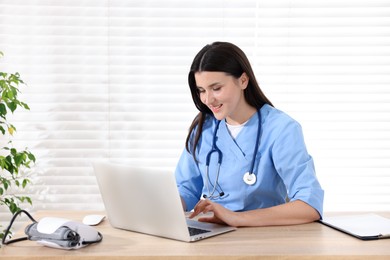 Photo of Nurse working on laptop at wooden table in clinic