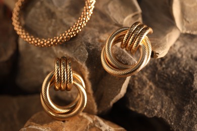 Photo of Stylish gold earrings and bracelet in smoke on rocks, closeup