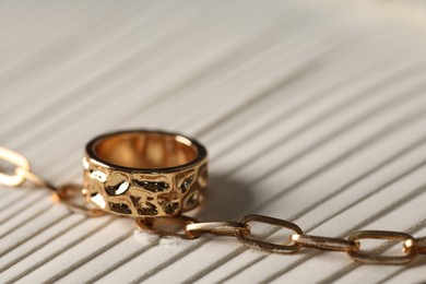 Photo of Stylish gold necklace and ring on sand, closeup. Space for text