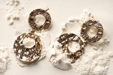 Photo of Stylish gold earrings on sand, top view