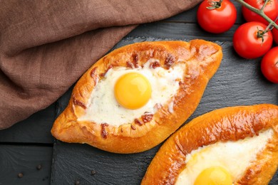 Photo of Tasty khachapuri with cheese, eggs and tomatoes on black wooden table, flat lay