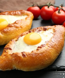 Photo of Tasty khachapuri with cheese and eggs on black wooden table, closeup