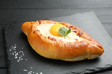 Photo of Tasty khachapuri with cheese, egg, salt and parsley on black table, closeup