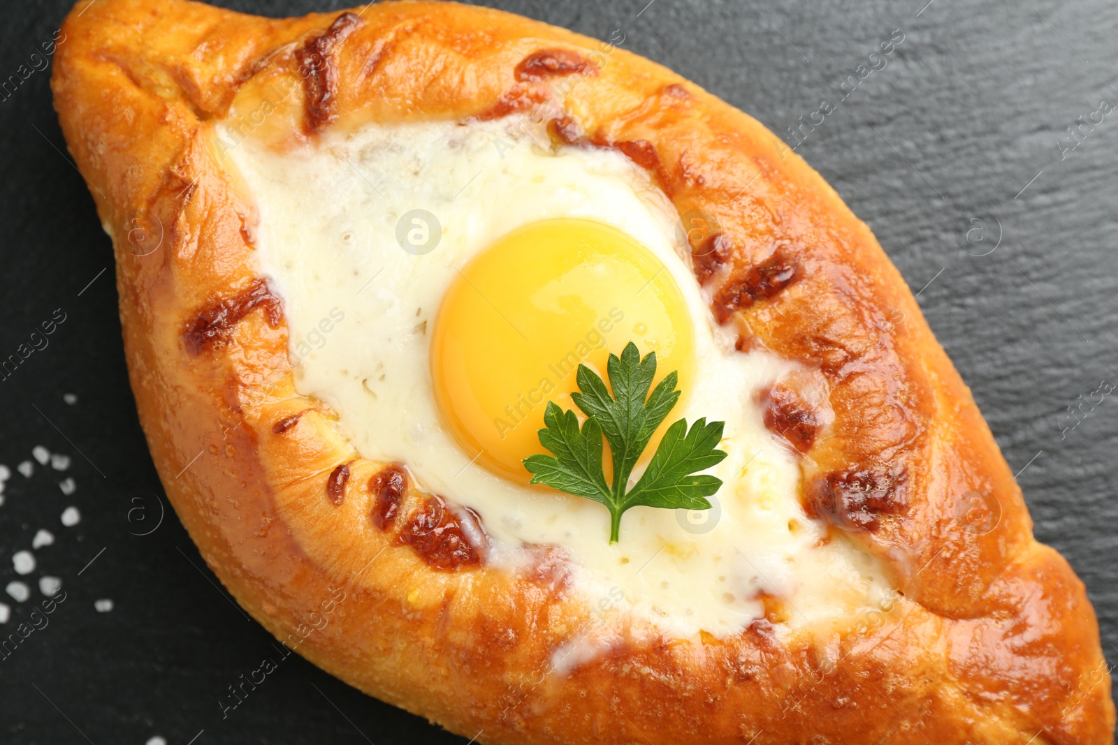 Photo of Tasty khachapuri with cheese, egg and parsley on black table, closeup