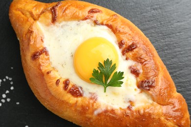 Photo of Tasty khachapuri with cheese, egg and parsley on black table, closeup