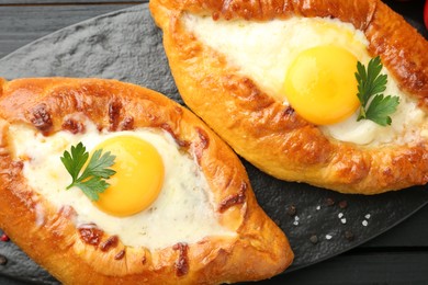 Photo of Tasty khachapuri with cheese, eggs and parsley on black table, above view