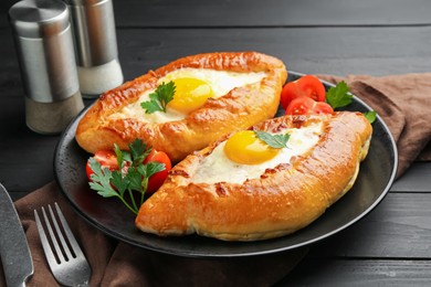 Photo of Tasty khachapuri with cheese and eggs served on black wooden table, closeup