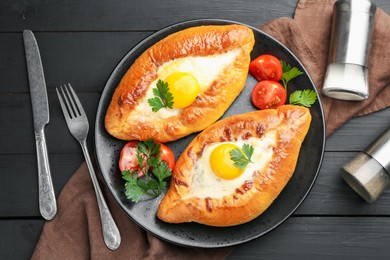 Photo of Tasty khachapuri with cheese and eggs served on black wooden table, flat lay